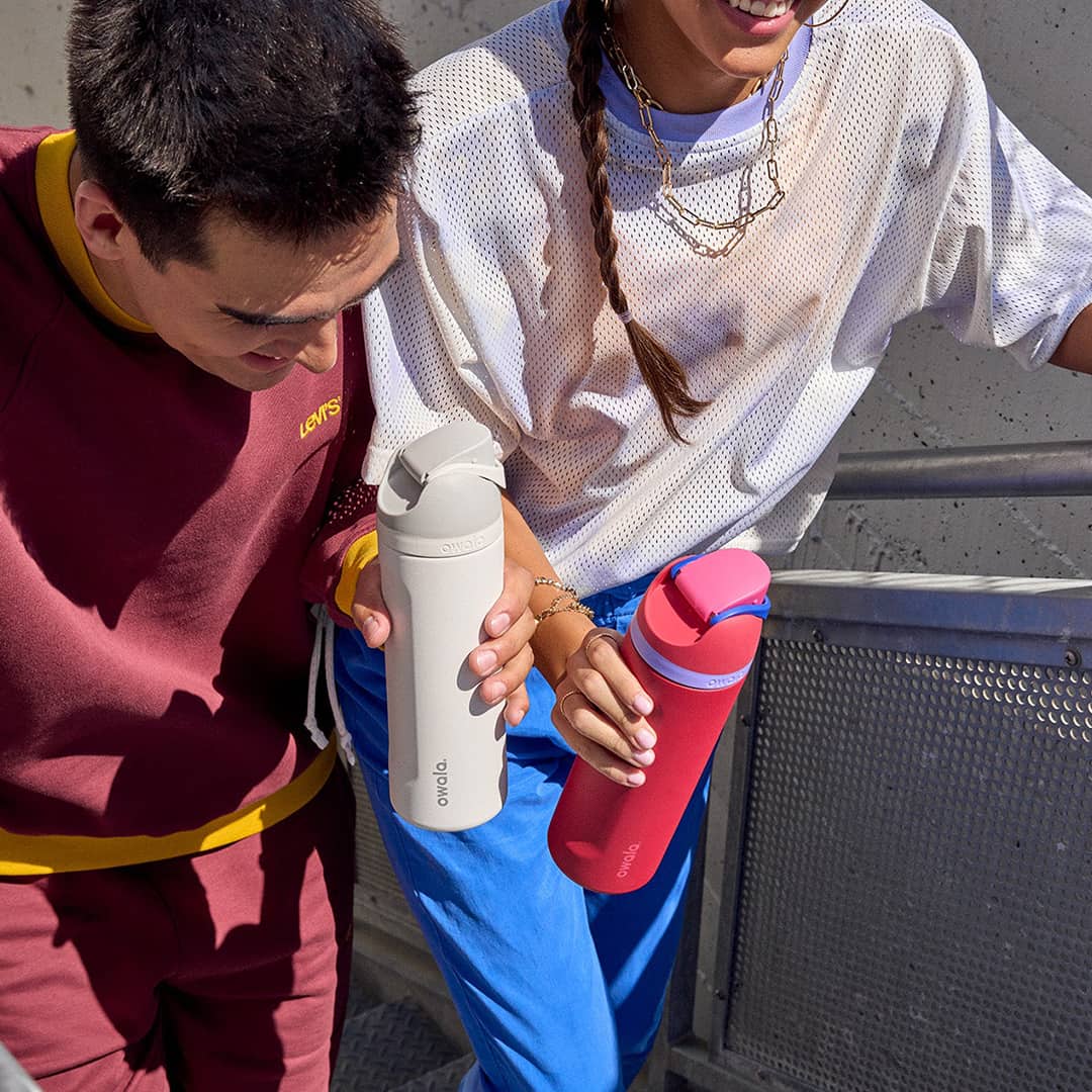 Two young people holding white and red Owala water bottles, displaying a range of colours available