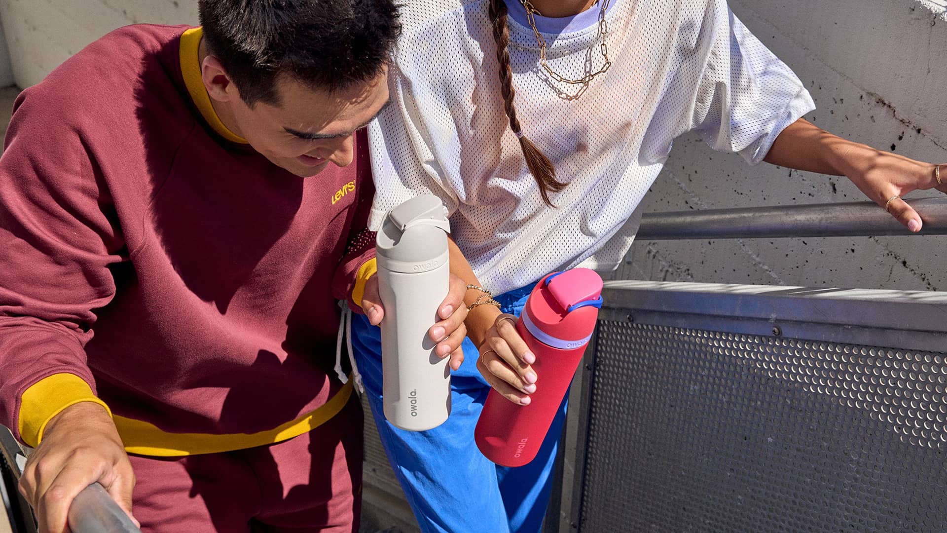 Two young people holding white and red Owala water bottles, displaying a range of colours available