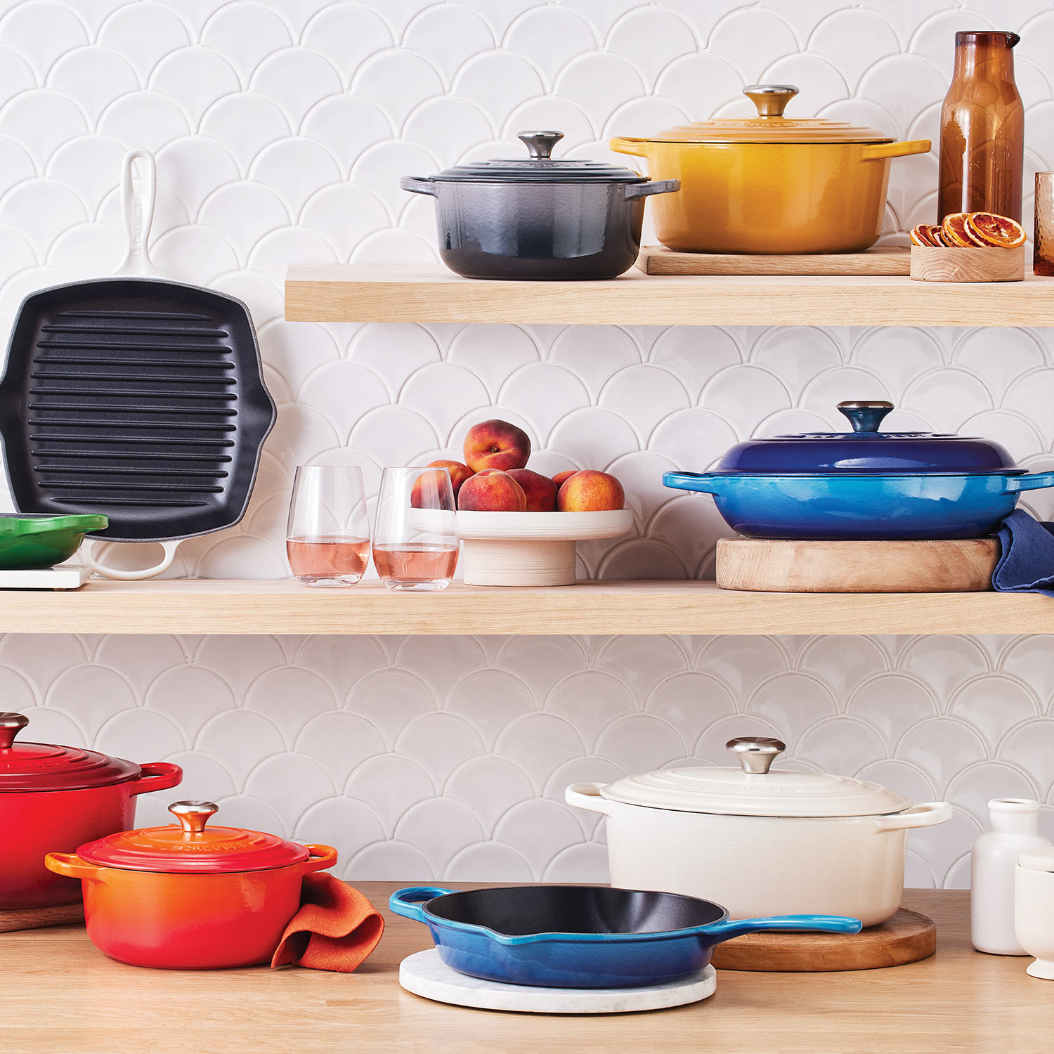 Colourful cookware and kitchen items displayed on wooden shelves with white tile background