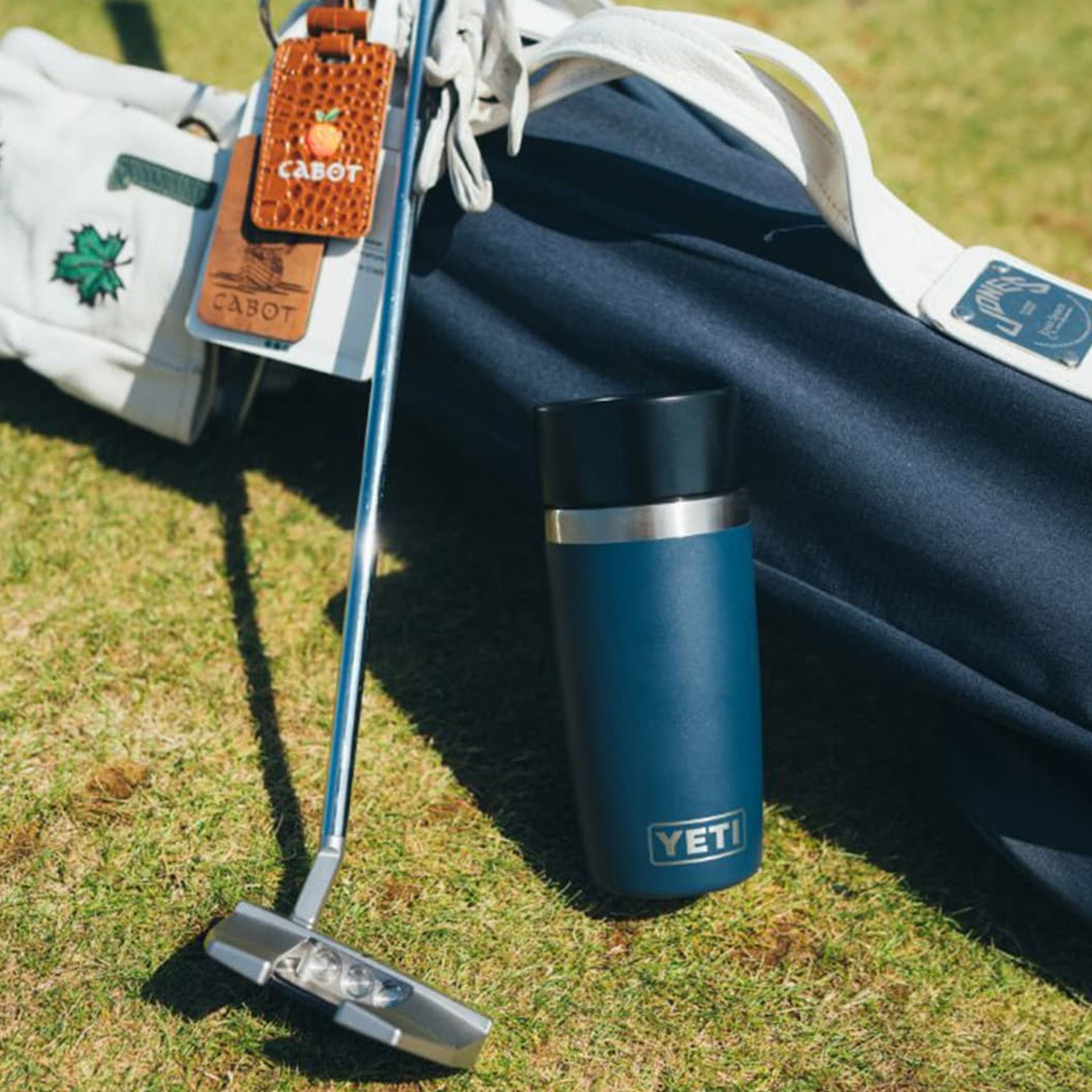Teal insulated water bottle with stainless steel band positioned next to car seat on grass outdoors.