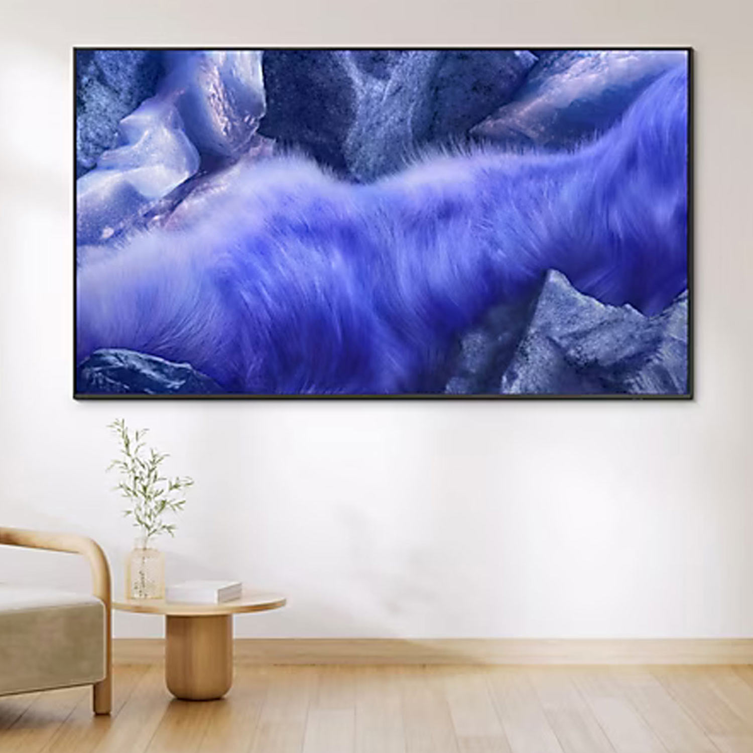Modern living room with cream armchair, wall-mounted television displaying blue wave imagery, wooden panelling and minimal décor.