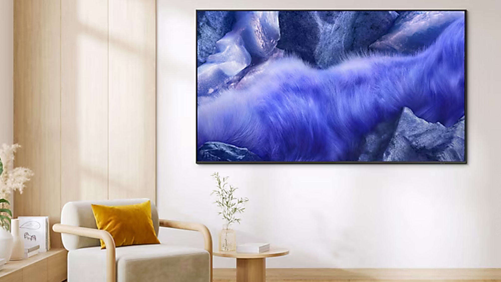 Modern living room with cream armchair, wall-mounted television displaying blue wave imagery, wooden panelling and minimal décor.