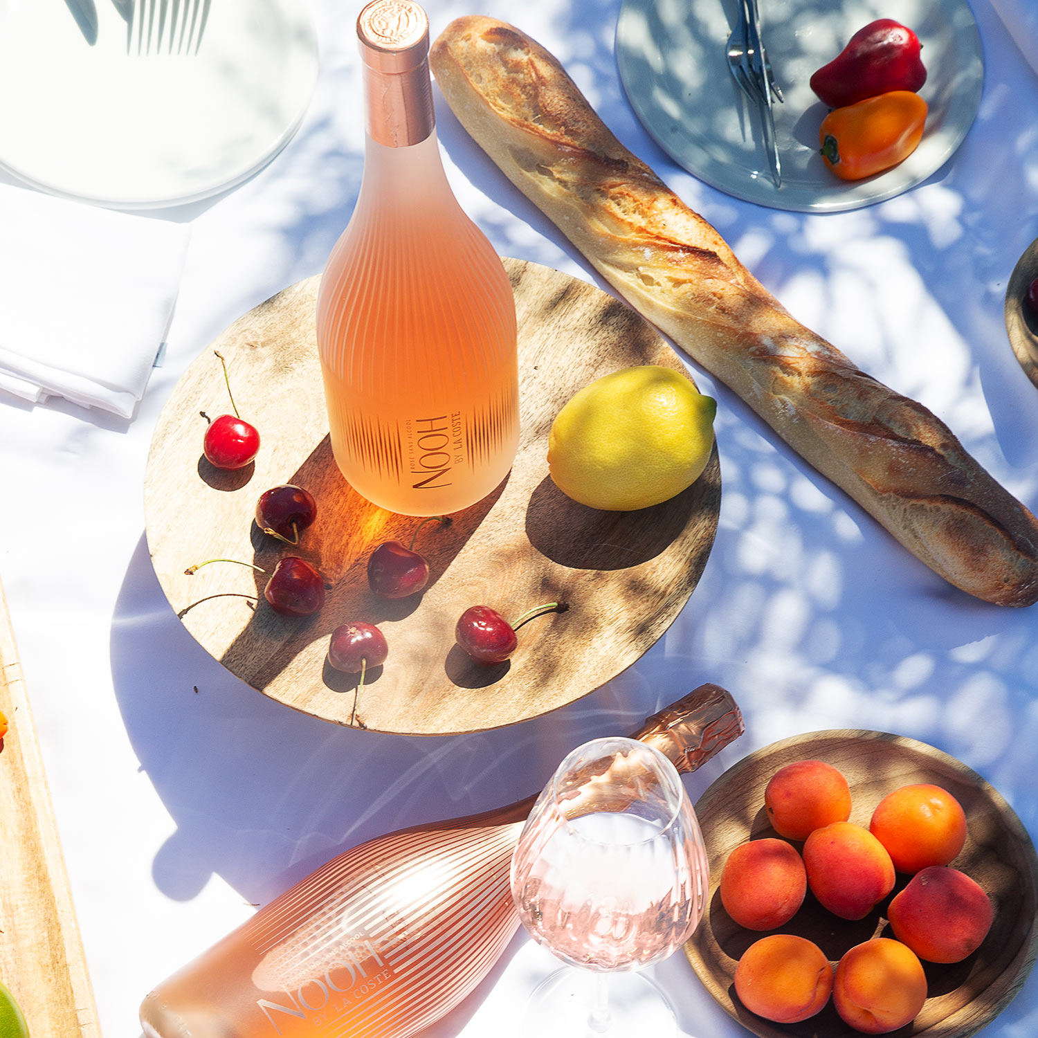 Summer spread featuring ros&eacute; wine, fresh bread, cherries, lemon, and peppers on wooden serving boards