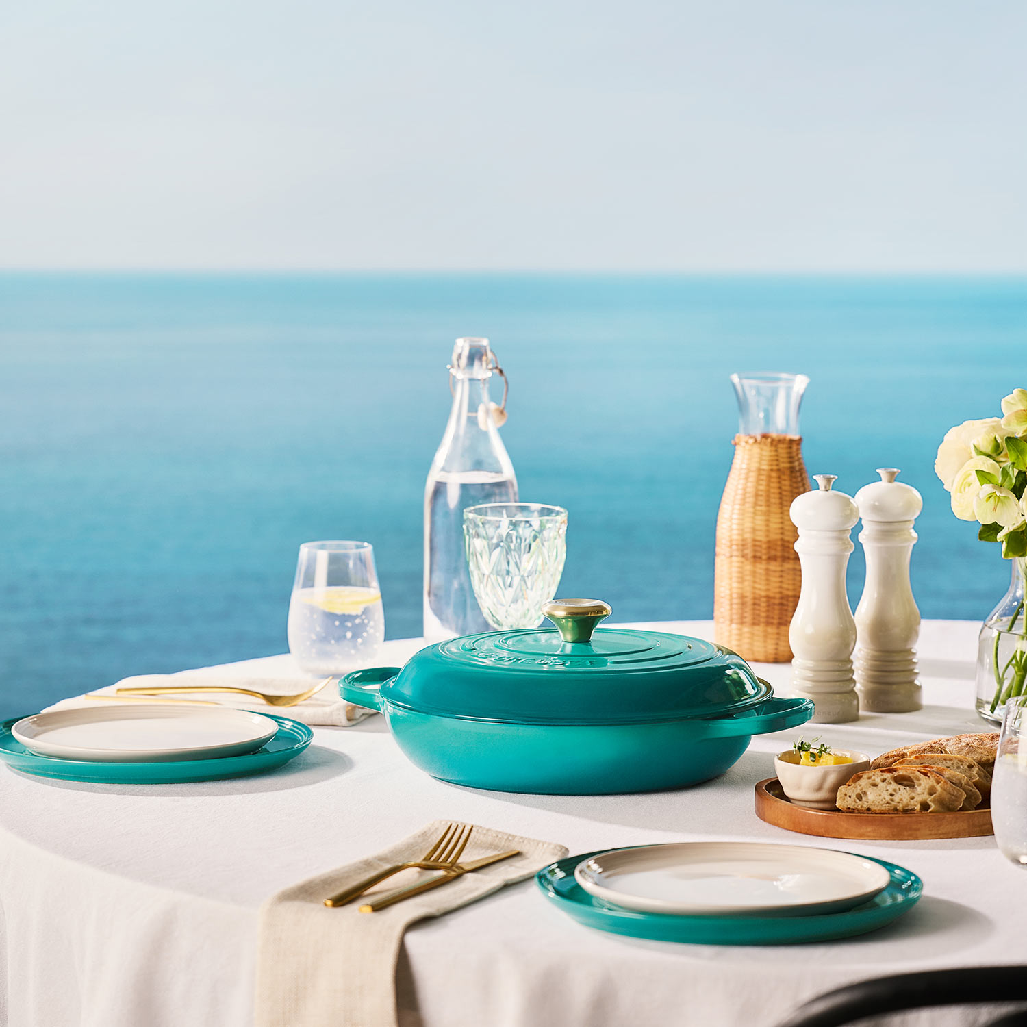 Coastal dining table setting with turquoise cookware, dinnerware, and glassware overlooking blue ocean view