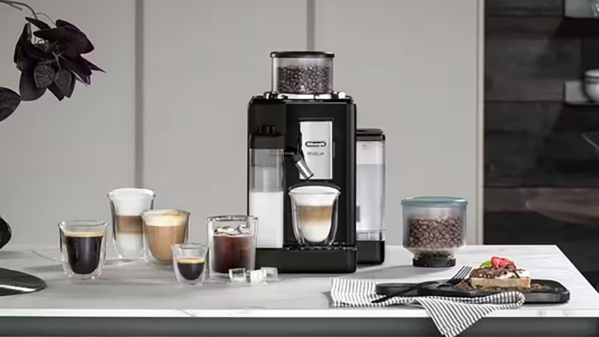 Black coffee machine with milk frother surrounded by various coffee drinks and coffee beans