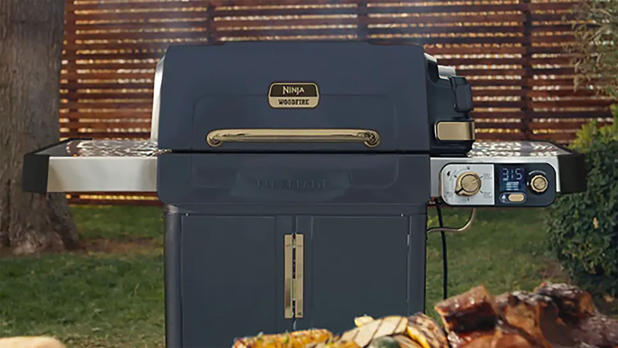 Navy Ninja Woodfire outdoor grill with grilled food and cooked meats in a garden setting