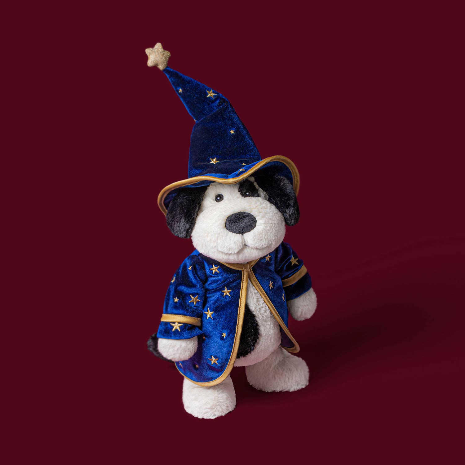 Soft toy dog wearing blue wizard hat and star-patterned coat against orange background