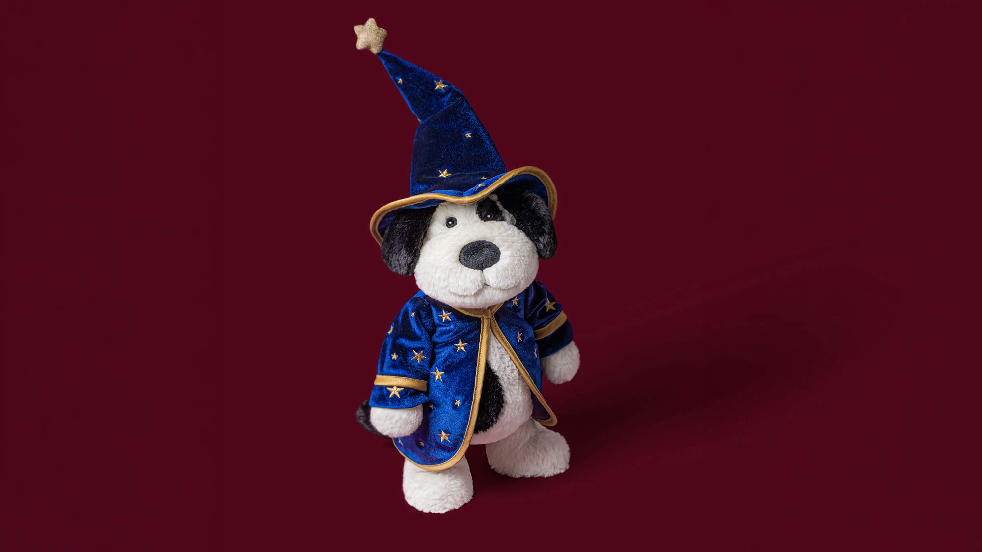 Soft toy dog wearing blue wizard hat and star-patterned coat against orange background