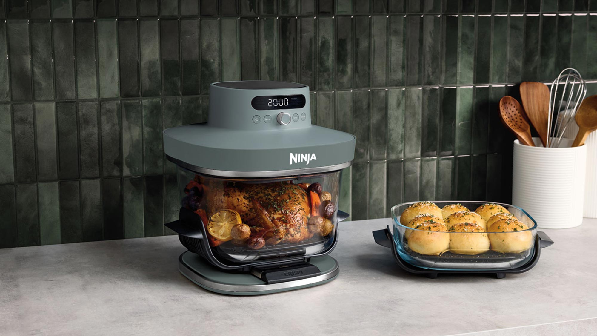 Ninja air fryer oven with roasted chicken and golden rolls displayed on kitchen bench with cooking utensils