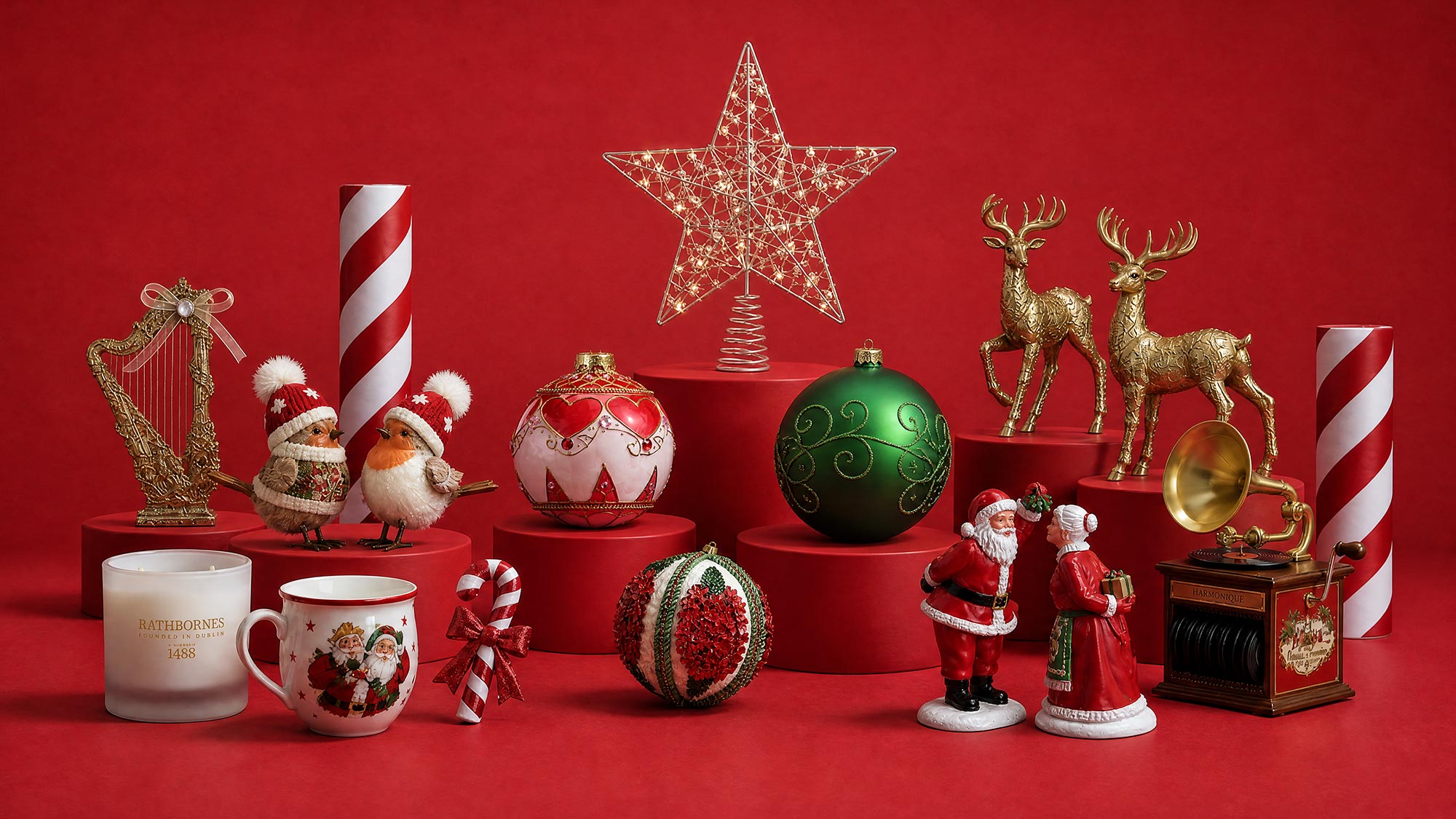 Christmas decorations collection including baubles, reindeer figurines, Santa figures, candles, and festive ornaments arranged on red display platforms