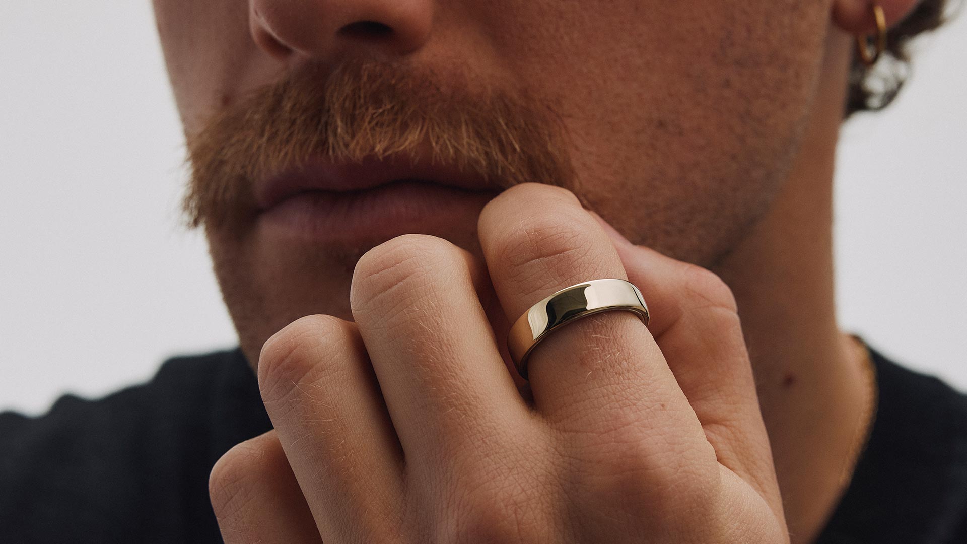 Man wearing polished gold Oura Ring on finger, demonstrating wellness tracking technology