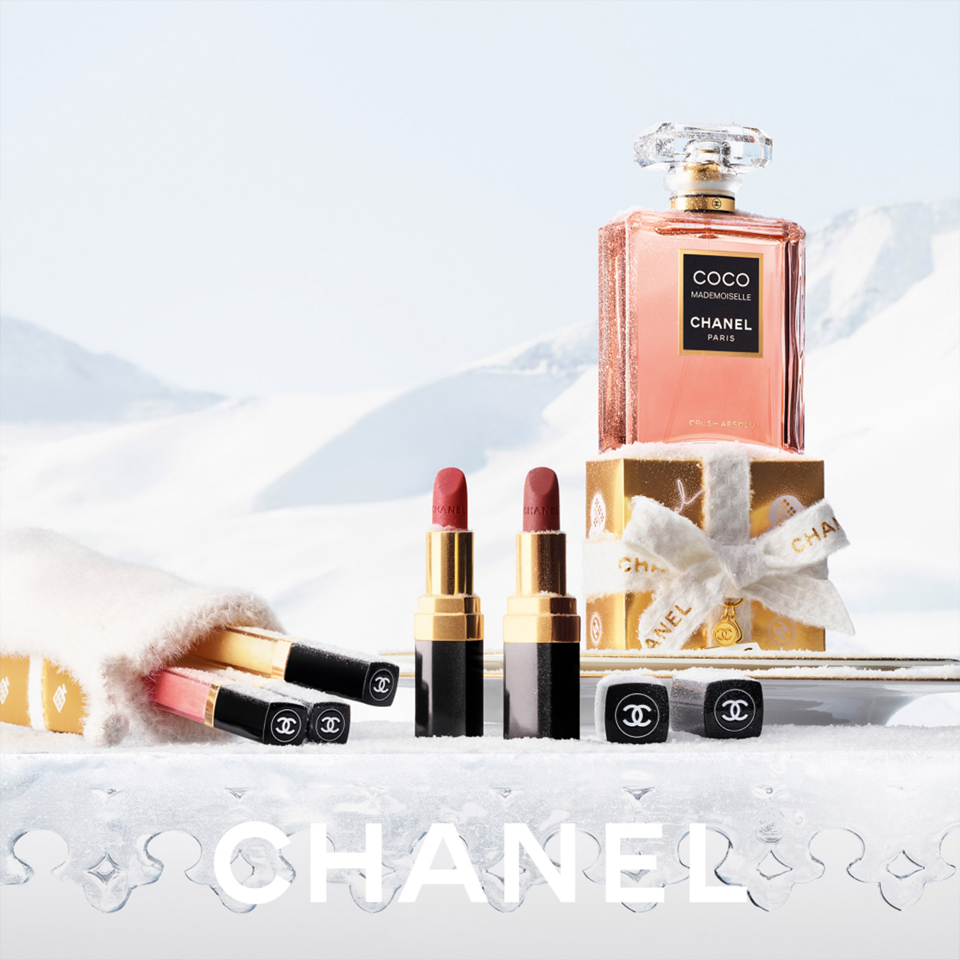 Chanel Coco Mademoiselle fragrance bottle surrounded by lipsticks and beauty products in snowy winter setting