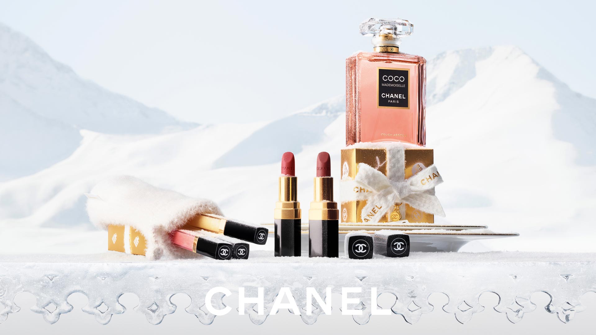 Chanel Coco Mademoiselle fragrance bottle with lipsticks and cosmetics displayed in snowy setting