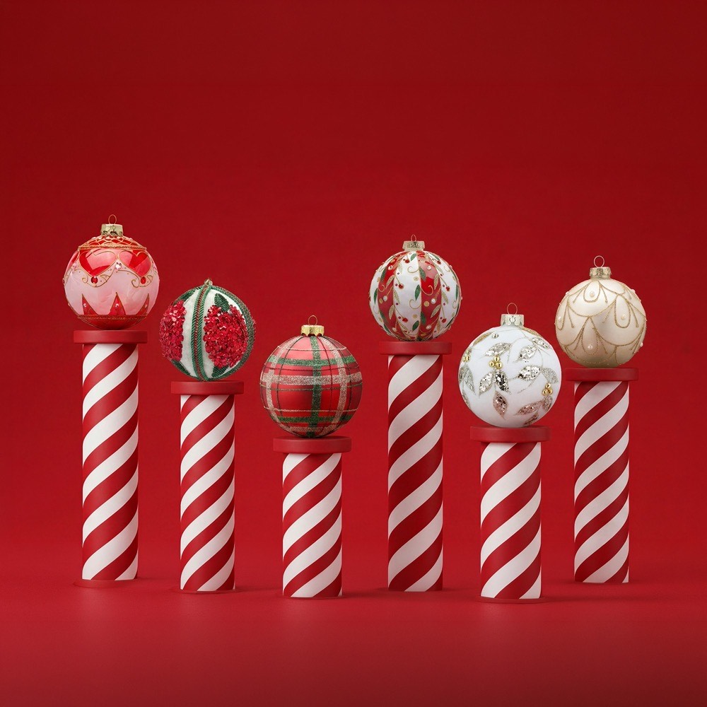 Six festive baubles in red, white, and cream tones on striped candy cane-style stands against red background