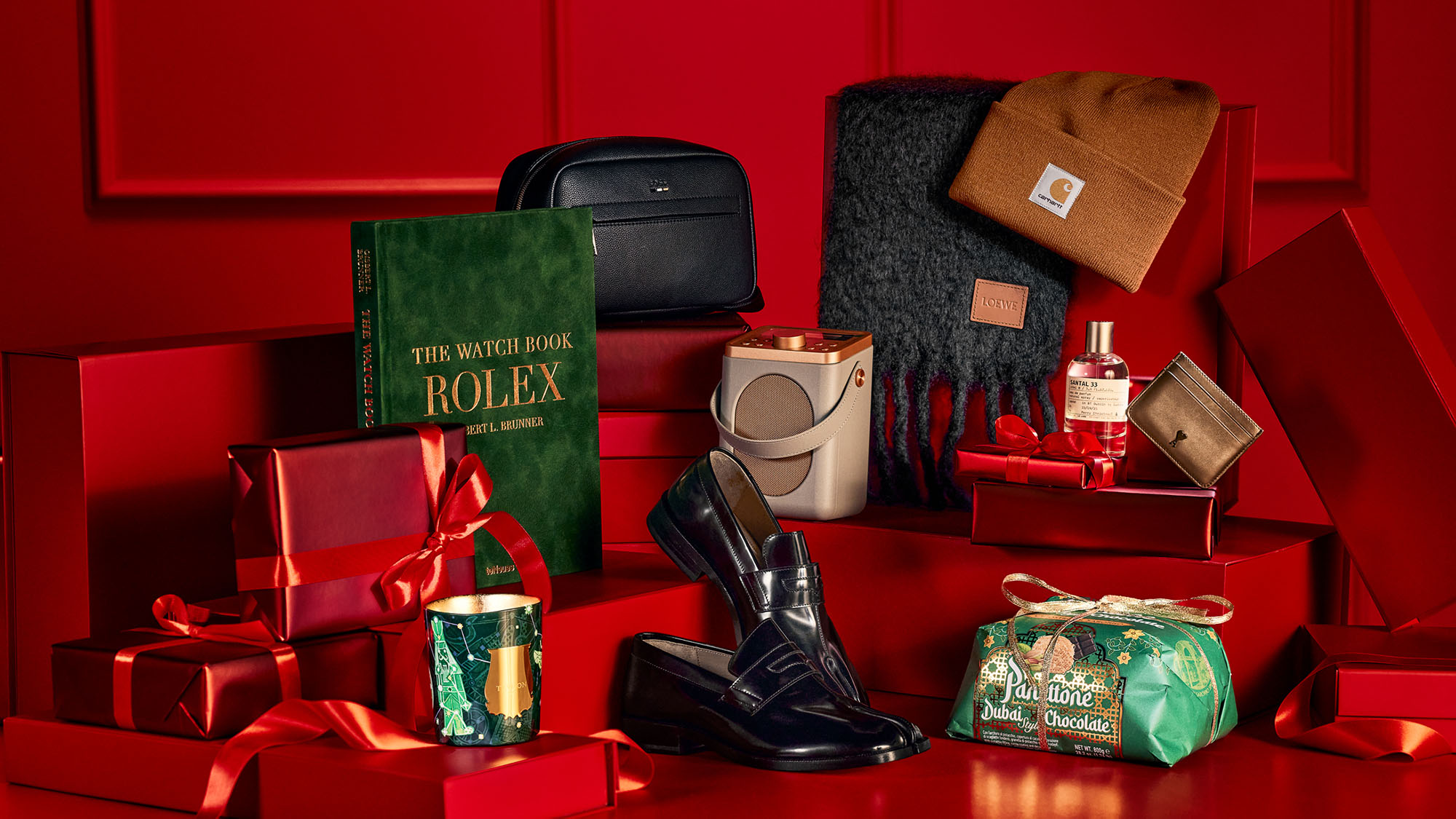 A festive display of luxury gifts on a red background, including a book, shoes, scarf, hat, and wrapped presents.