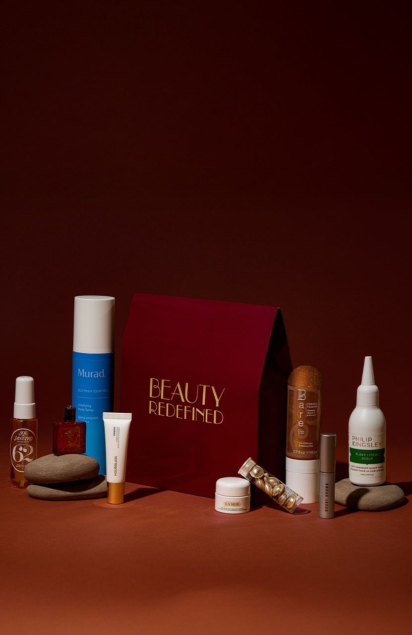 A collection of beauty products is arranged around a red bag labeled 'Beauty Redefined' on a dark background.