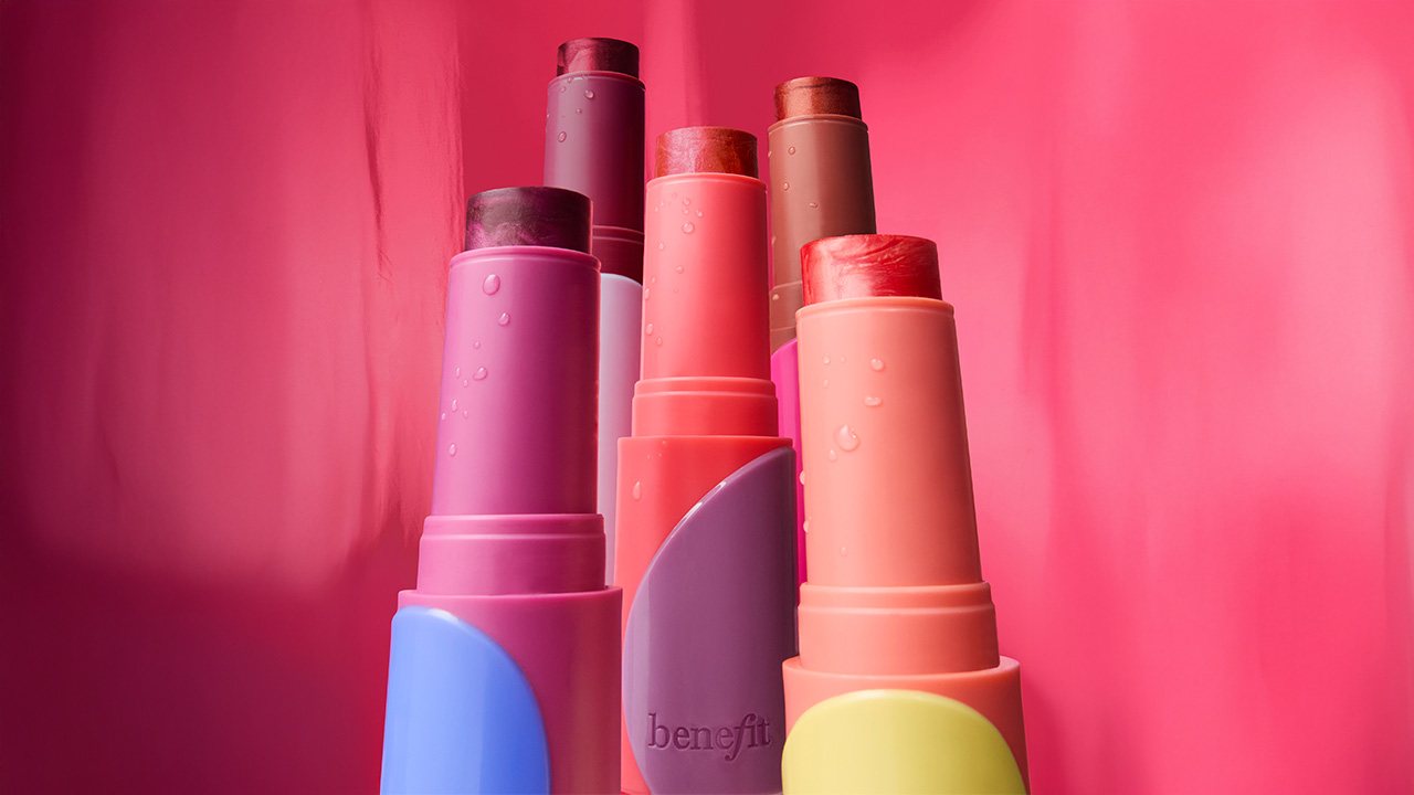 Colorful lipstick tubes in various shades against a vibrant pink background.