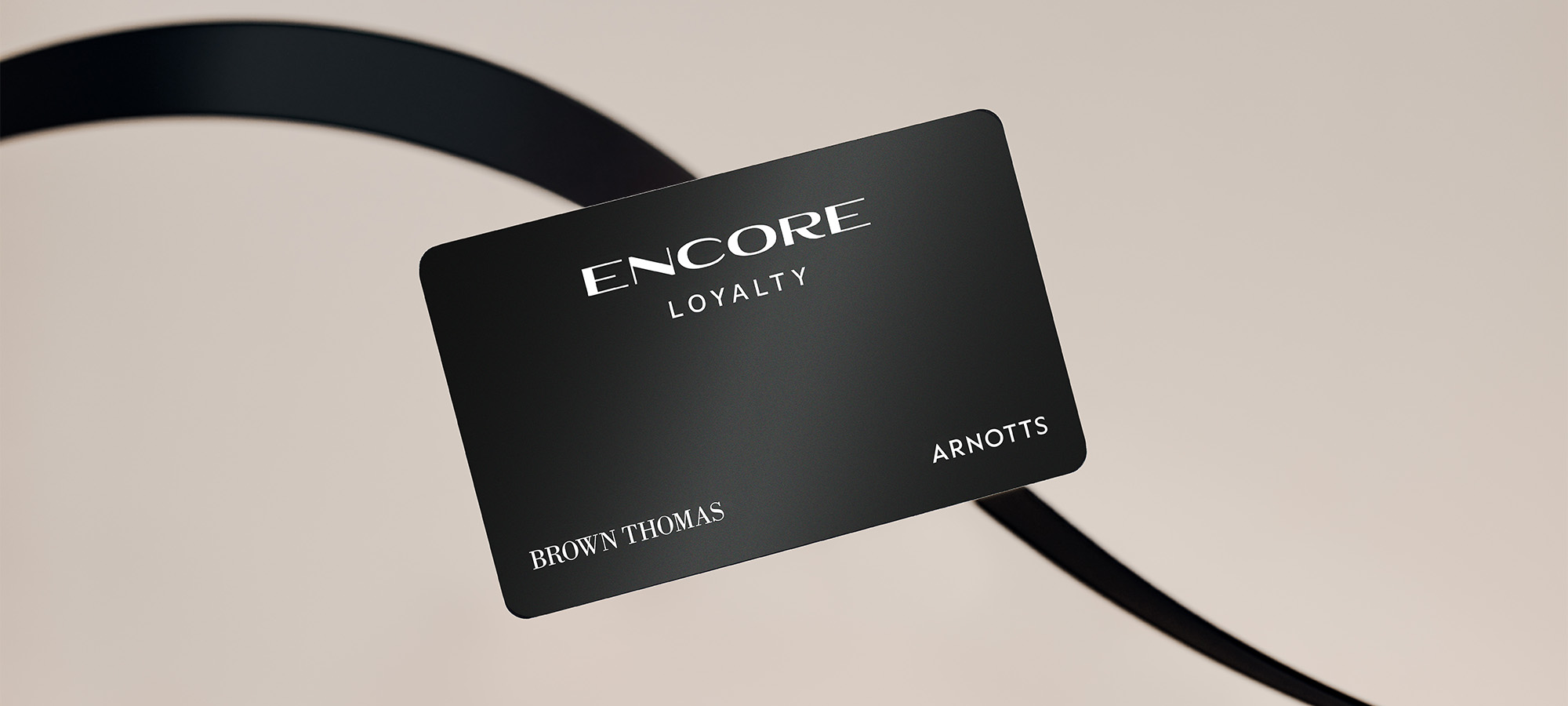 A black loyalty card titled 'Encore' with 'Brown Thomas' and 'Arnotts' against a beige background, intersected by a black ribbon.