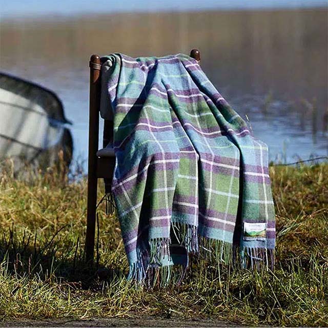 A plaid blanket draped over a chair by the lakeside, with a boat in the background.