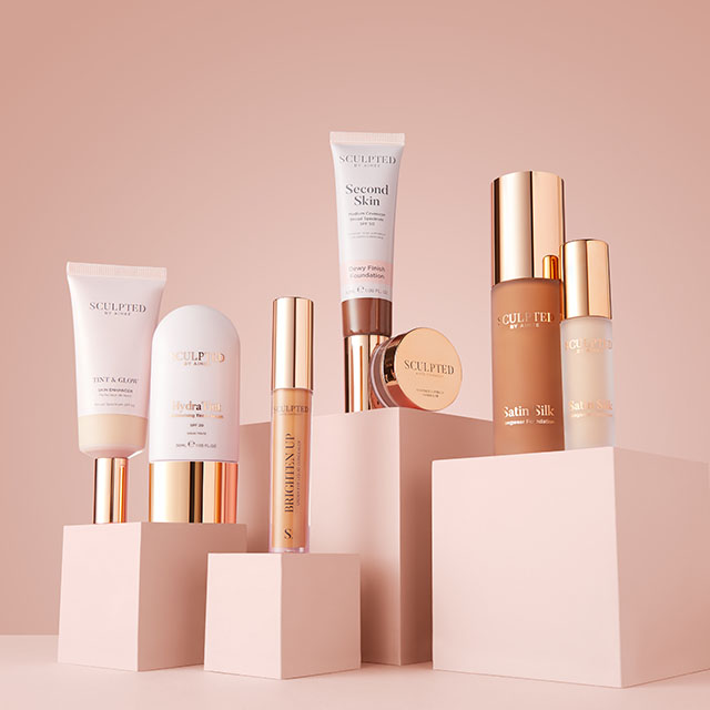 A collection of skincare and makeup products with gold accents displayed on pastel pink blocks.