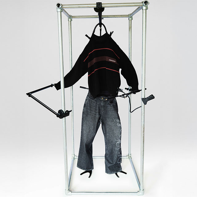 A black sweater and jeans are mounted on a metal frame with adjustable arms, resembling a human figure.