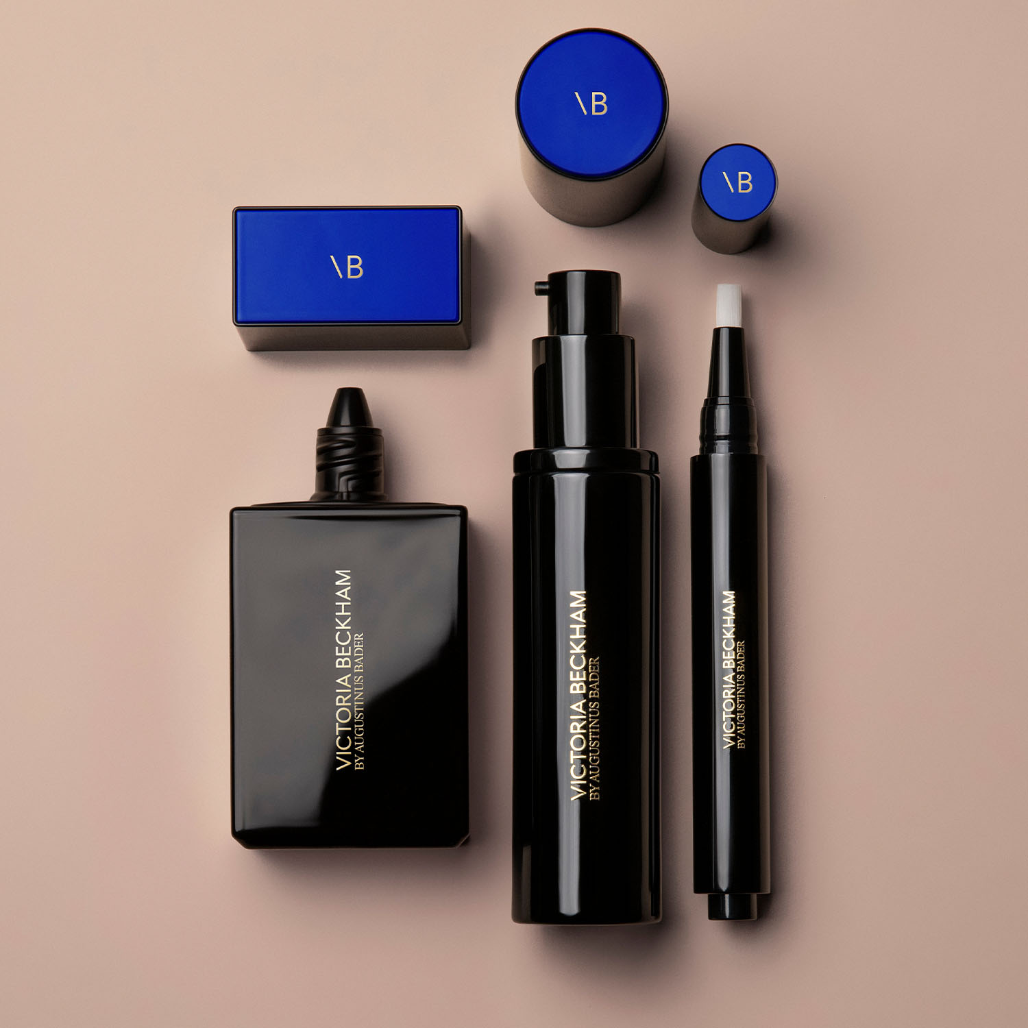 A set of Victoria Beckham beauty products featuring sleek black packaging with blue accents, arranged on a beige surface.