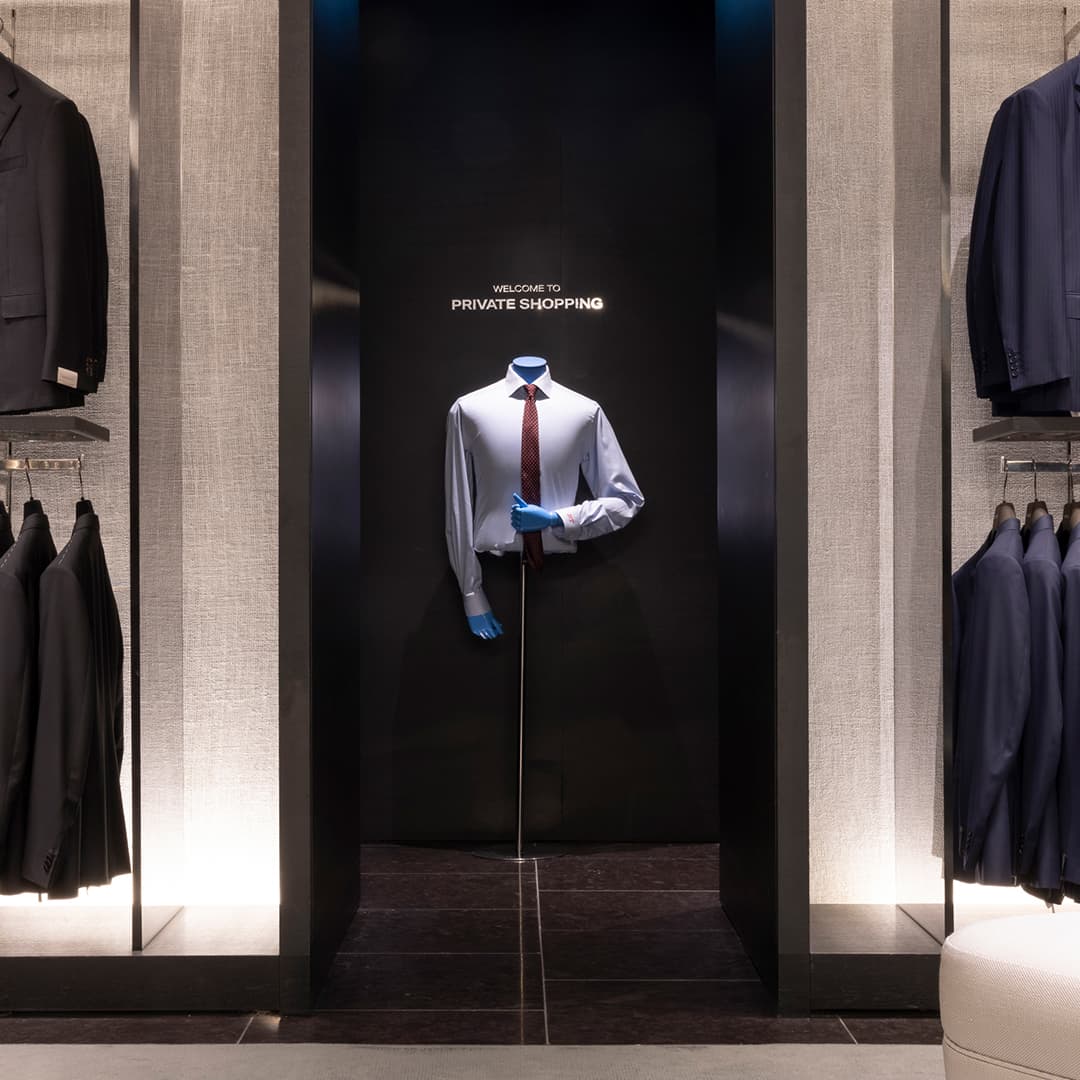 A clothing store display featuring a mannequin with a shirt and tie, surrounded by racks of suits.