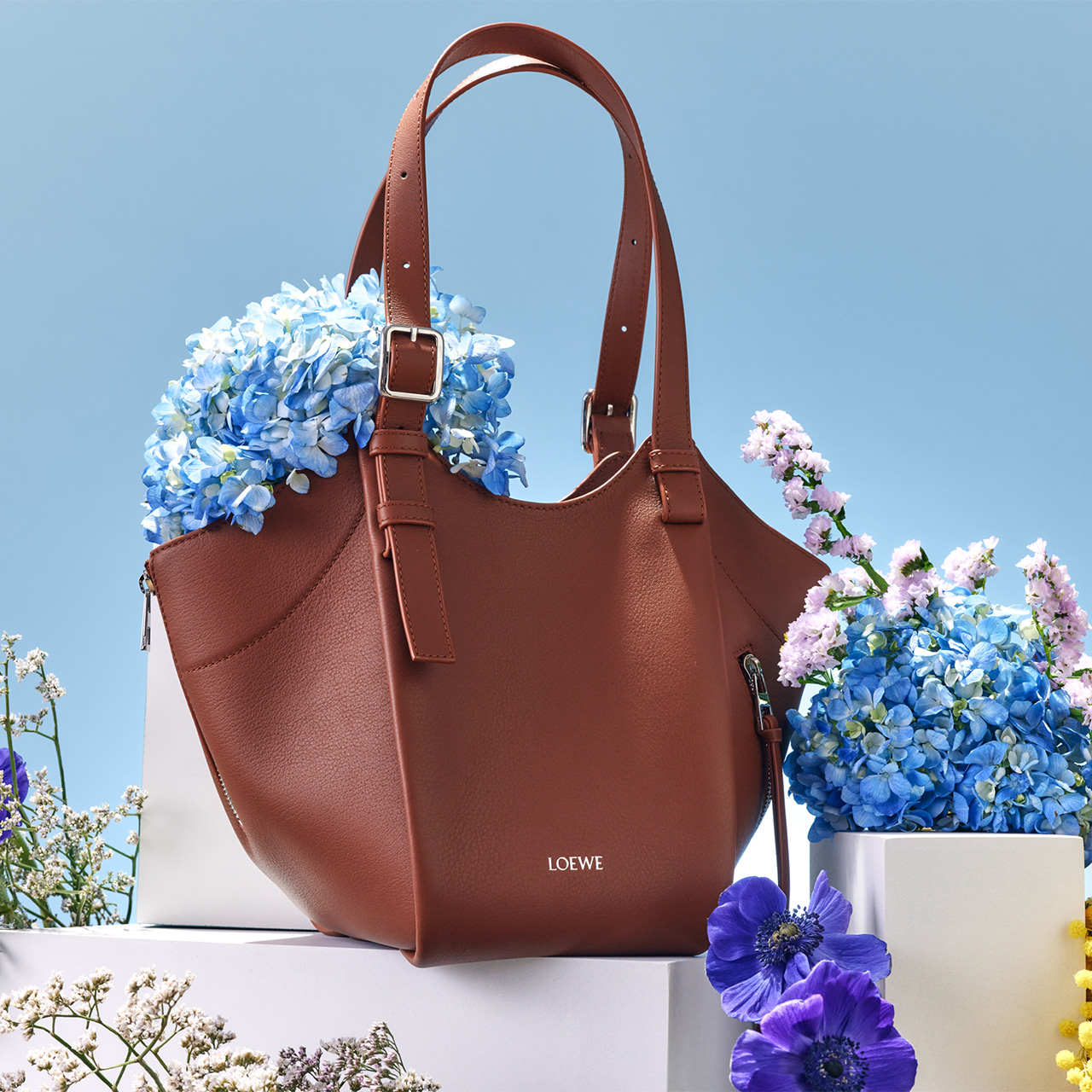 A brown Loewe handbag is adorned with vibrant blue and purple flowers.
