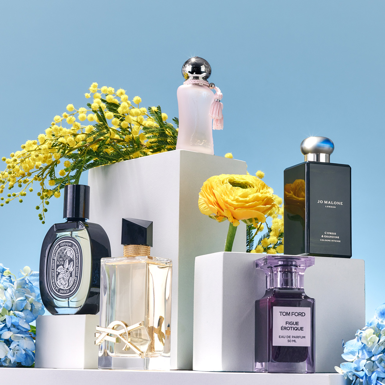 Perfume bottles displayed on white blocks with yellow and blue flowers, set against a blue background.