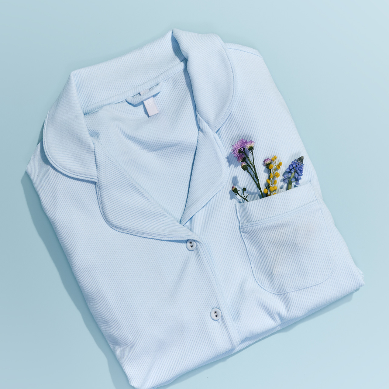 Folded light blue shirt with small flowers in the pocket on a light blue background.