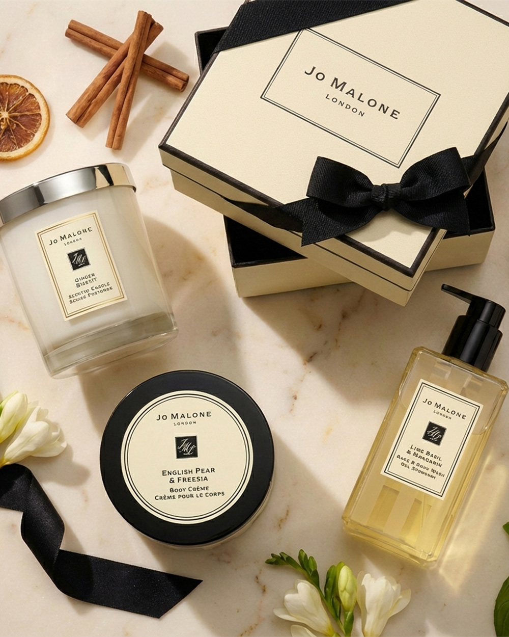 A set of Jo Malone products on a marble surface WITH dried orange slices and cinnamon.