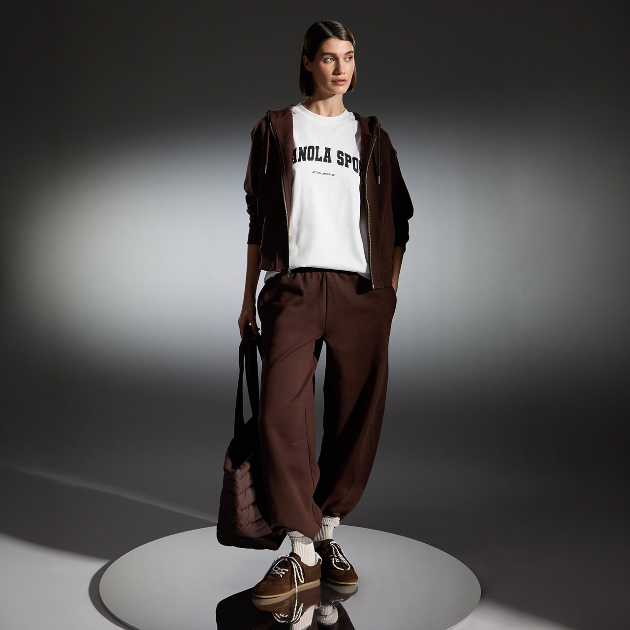 Woman wearing brown loungewear set with zip hoodie and wide-leg trousers, paired with white socks and tan shoes