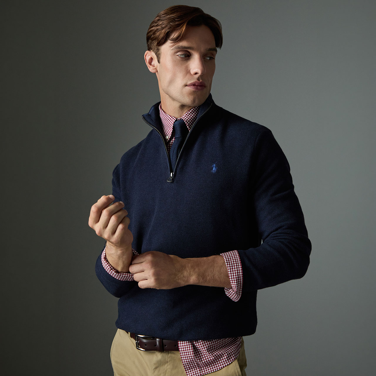 Man wearing a navy quarter-zip knit with embroidered logo, layered over a burgundy checked shirt and tie