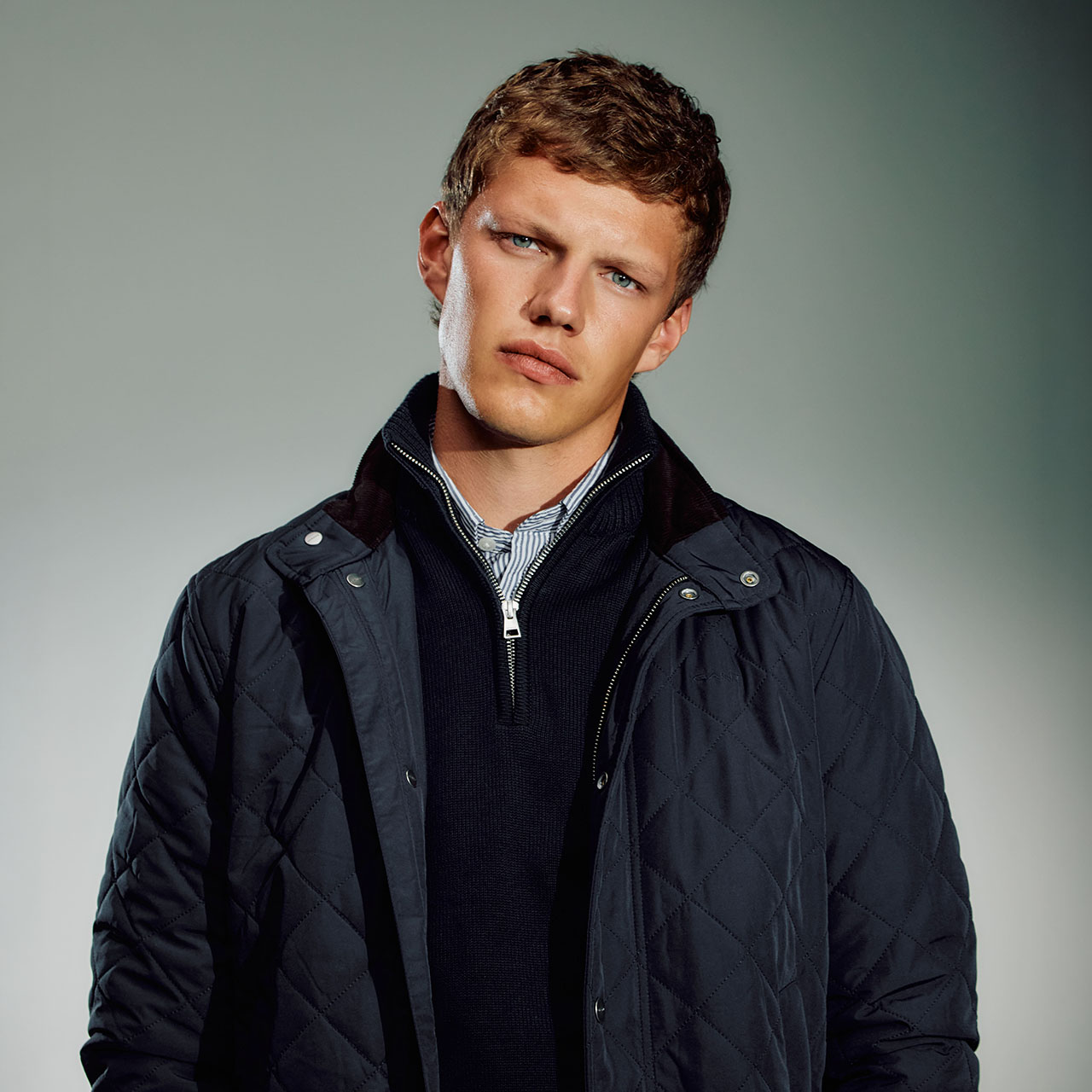 Man wearing a navy quilted jacket with collar, paired with a navy knit and checked shirt underneath