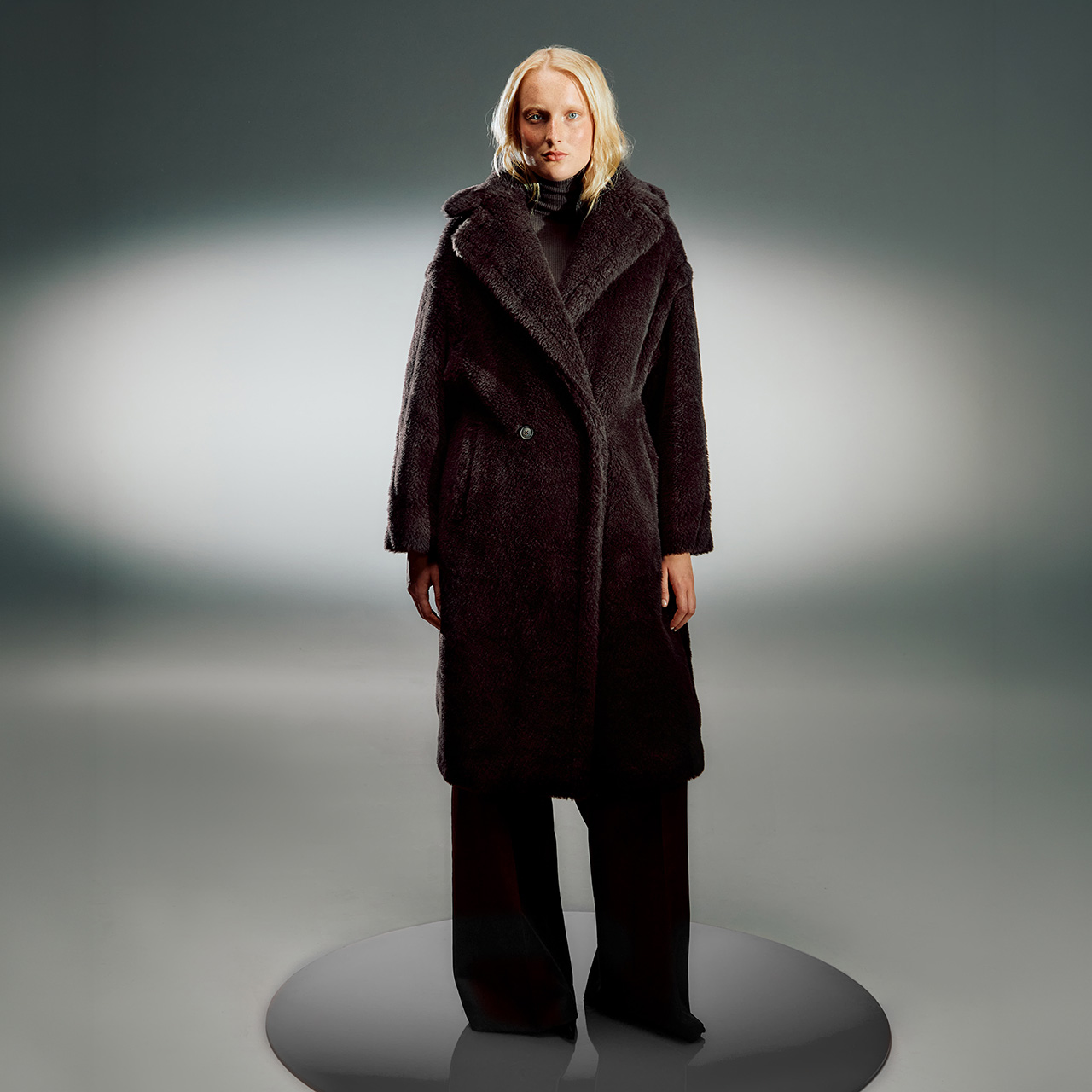Woman wearing a dark textured wool coat with oversized collar and single button fastening over a black turtleneck