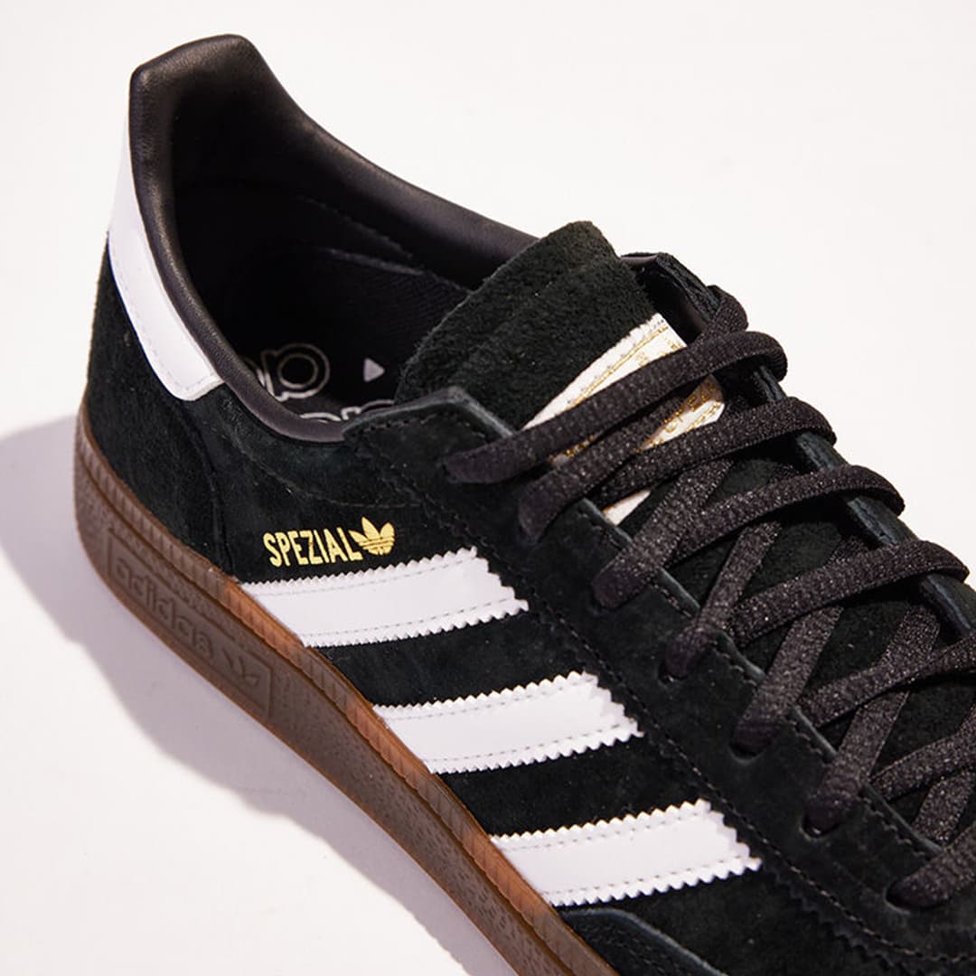 Black suede Adidas Spezial trainer with white stripes and brown gum sole, shown in close detail