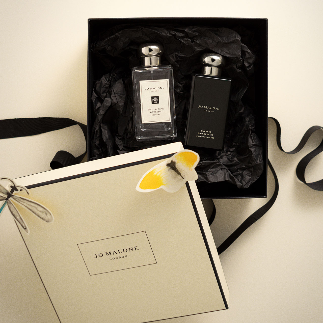 Jo Malone fragrance gift set in black box containing two perfume bottles with black ribbon, packaging and white daisy decoration.