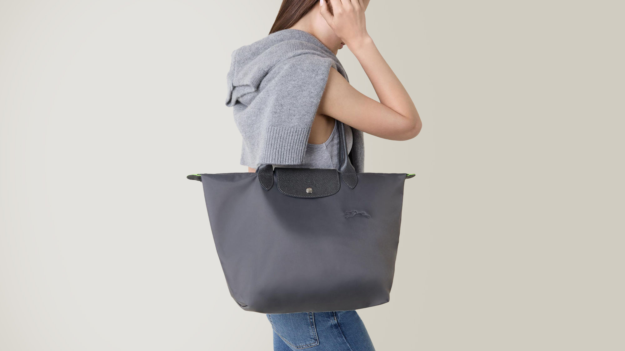 A person wearing a sleeveless top and jeans holds a large gray tote bag while walking.