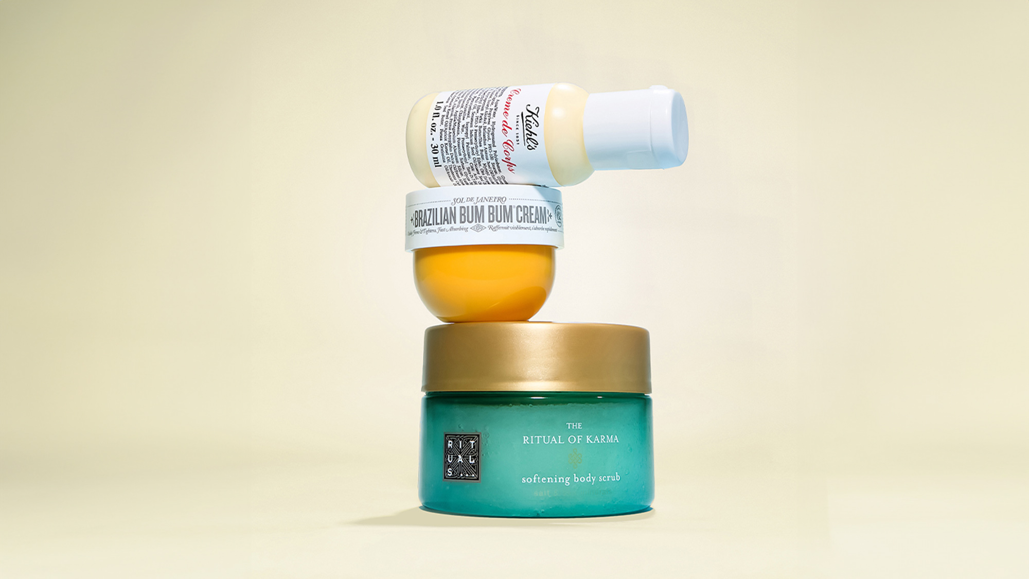 Three skincare products stacked: a bottle on top of a jar labeled 'Brazilian Bum Bum Cream,' which sits on a green jar 'The Ritual of Karma.'