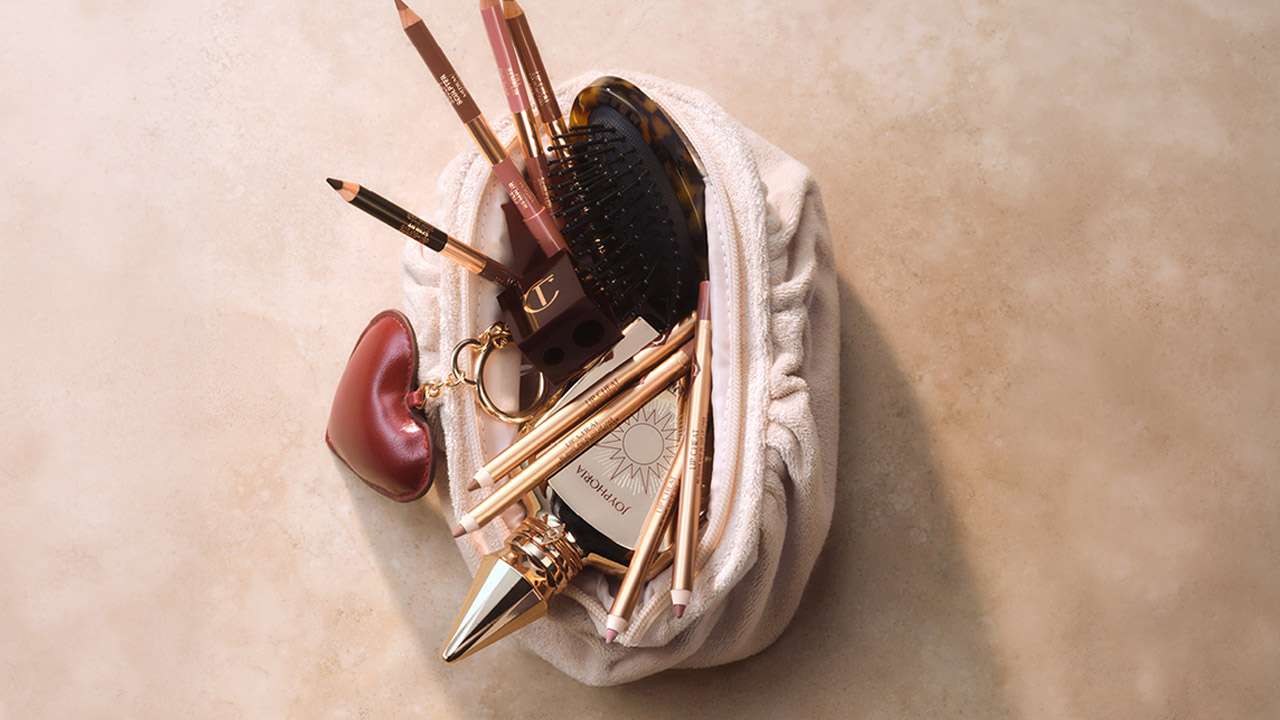 Bridal beauty products arranged on white fabric: makeup brushes, eyeliner pencils, black hair comb, pink ear-shaped ornament, gold pen, and skincare bottle with sun logo
