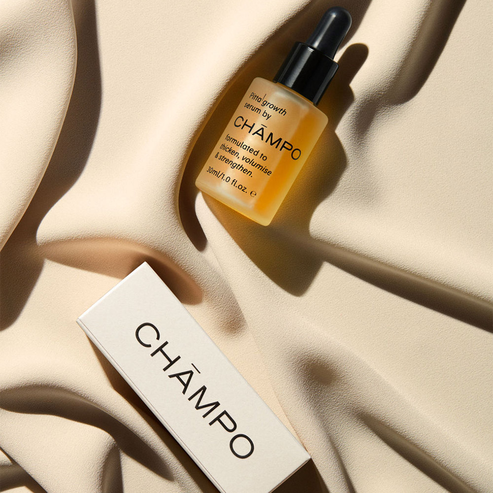 Golden hair growth serum bottle and white product tube labelled Champo on neutral beige background with shadow