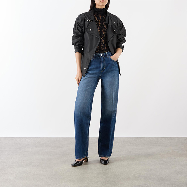 Person in a black jacket, lace top, and blue straight jeans, standing against a plain background.