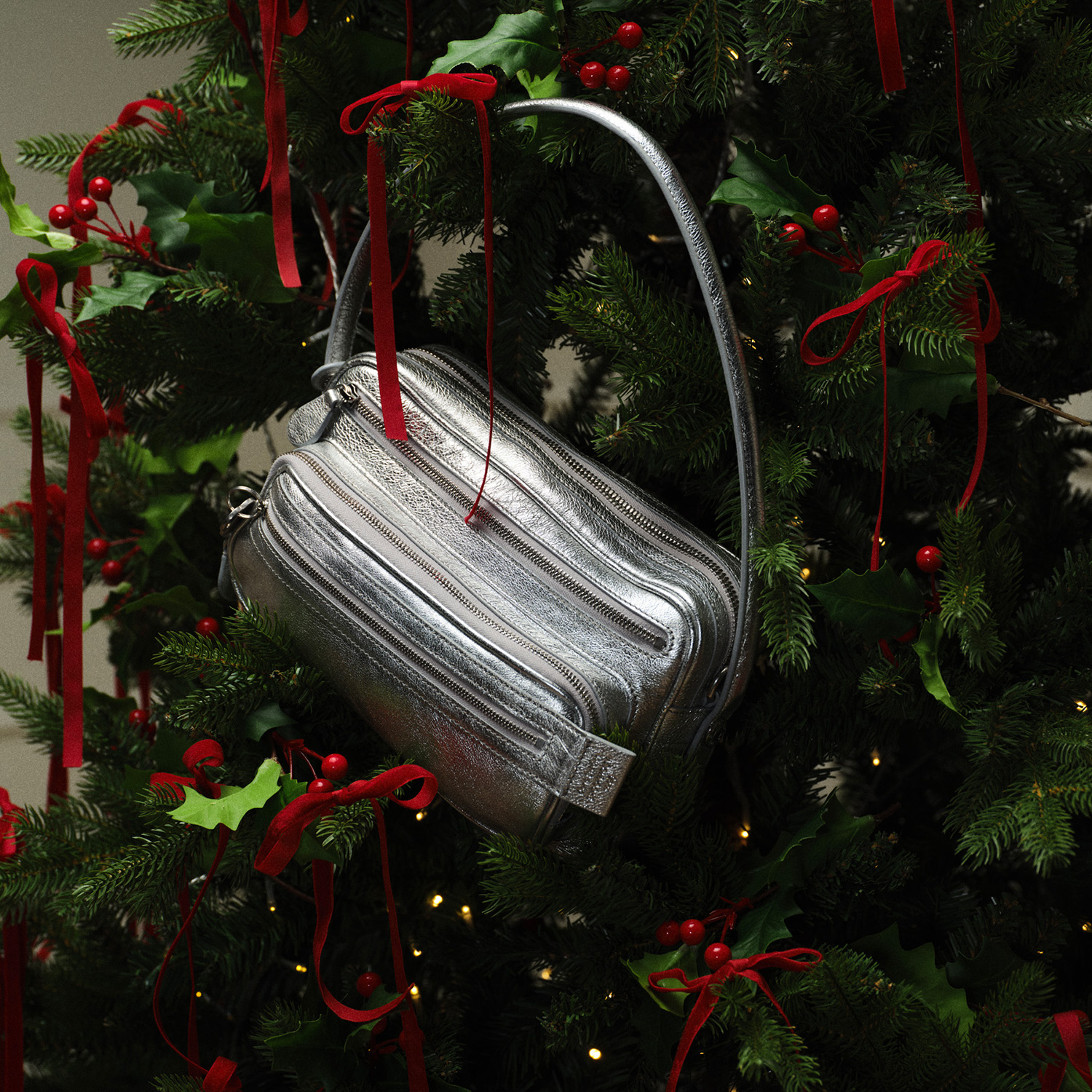 A silver handbag hangs on a decorated Christmas tree with red ribbons and lights.