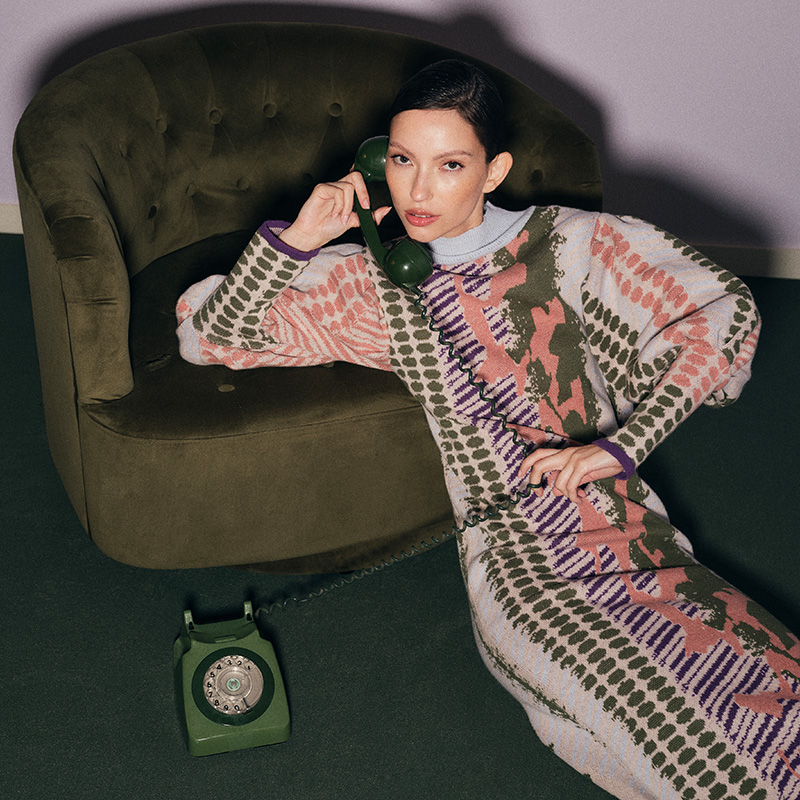 A person in a patterned dress sits on a green chair, holding a green rotary phone to their ear.
