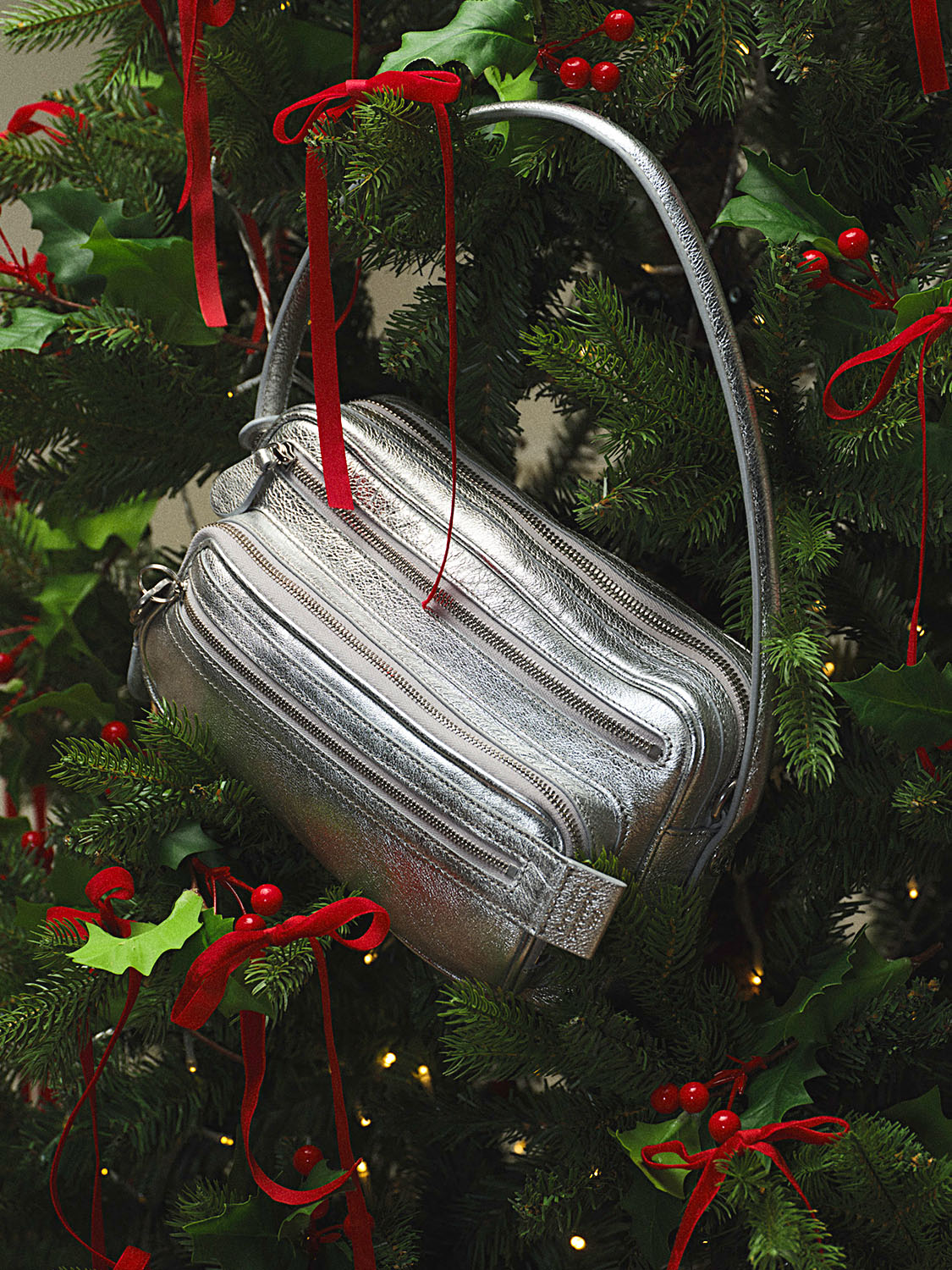 A silver handbag hanging on a Christmas tree decorated with red ribbons and holly.