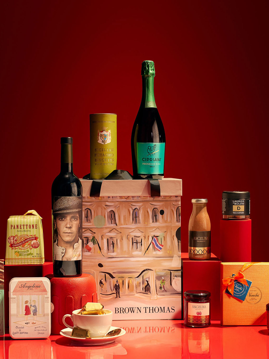 Assorted gourmet gifts and packages, including bottles and tins, arranged against a red background.