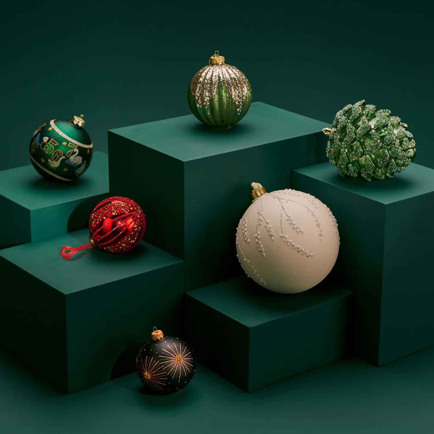 Colorful Christmas ornaments displayed on dark green geometric blocks.

