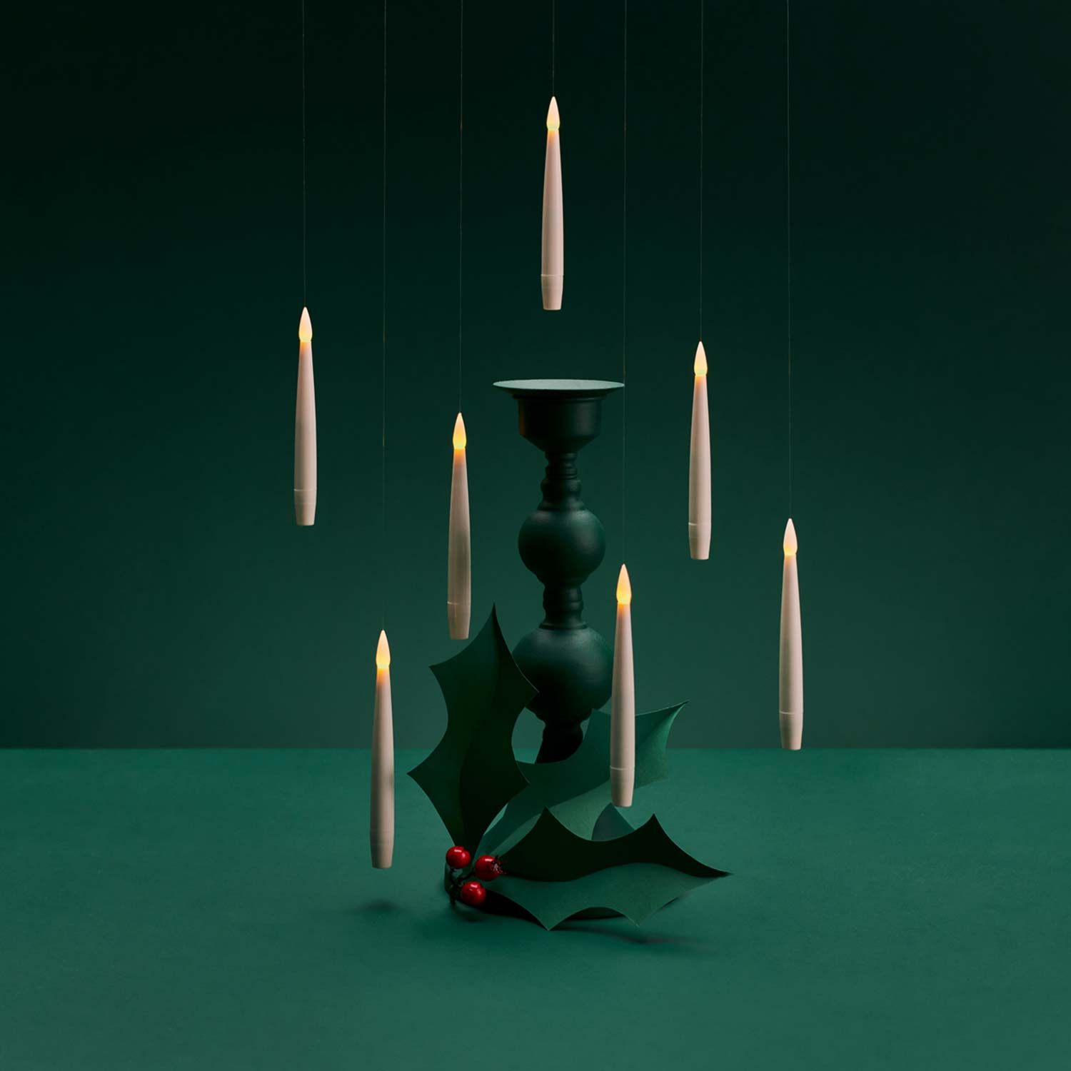 Floating candles surround a candle holder with holly leaves and berries on a dark green background.