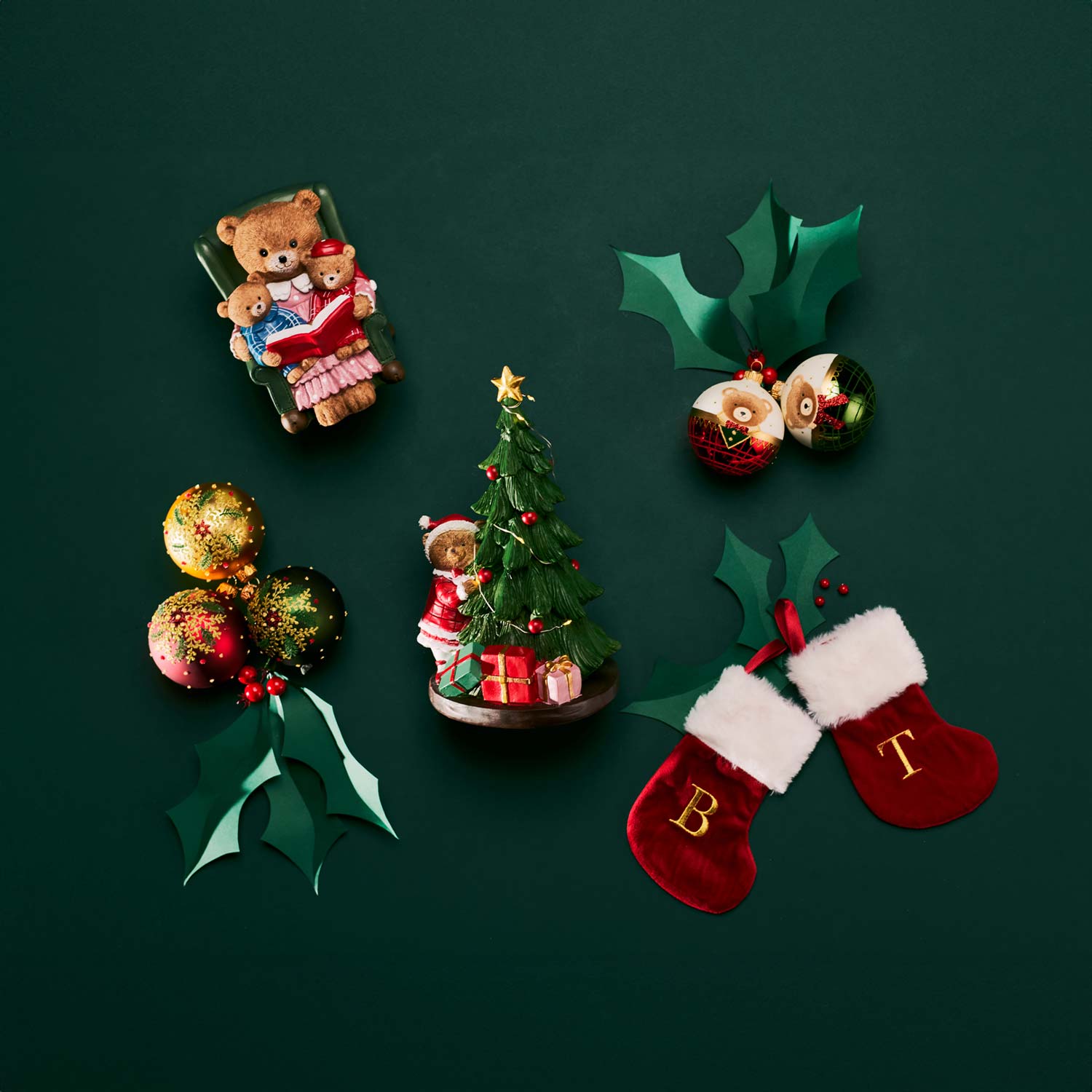 Christmas decorations including stockings with initials, holly, teddy bear ornaments, and a small Christmas tree on a green background.