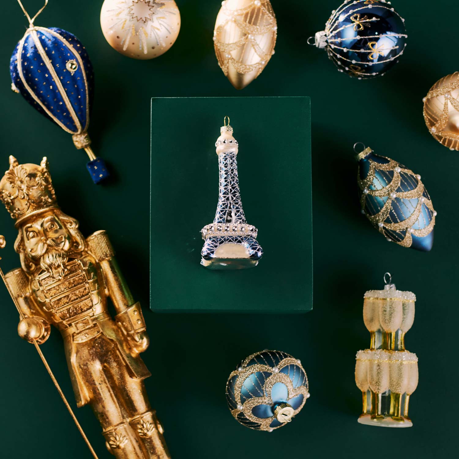 A collection of festive ornaments including a gold nutcracker, Eiffel Tower, and various spherical decorations on a green background.
